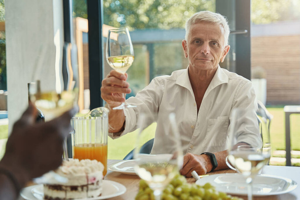 Man holding glass of wine while sitting at table - Foto, afbeelding