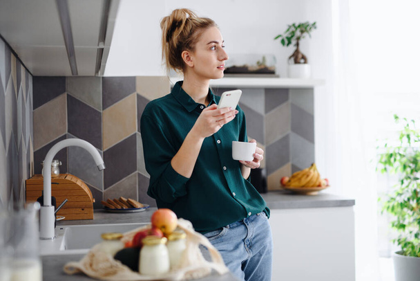 Portrait of young woman student with coffee at home, using smartphone. - Fotografie, Obrázek