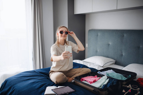 Portrait of young woman taking selfie indoors at home, planning holiday. - Photo, Image