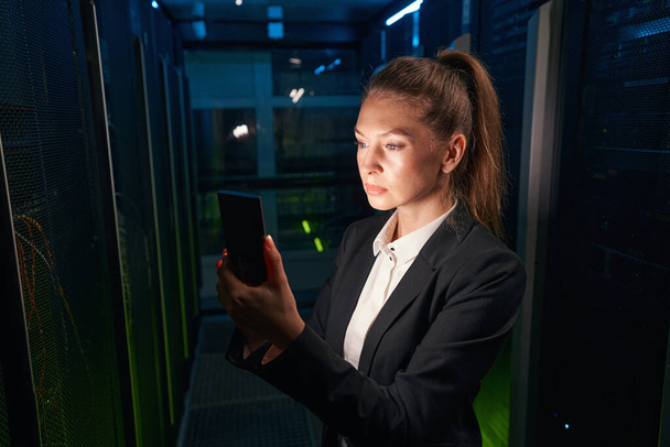 Técnico femenino trabaja en celular en centro de datos - Foto, Imagen