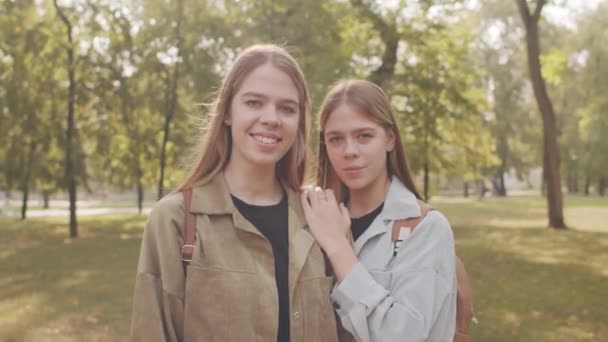 ポートレートショットとともにハンドヘルド追跡幸せな若い双子姉妹posingのためにカメラで公園で晴れた夏の日 - 映像、動画