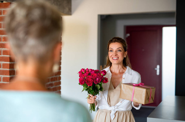 Happy adult daughter bringing gift and bouquet to senior mother indoors at home. - Fotoğraf, Görsel