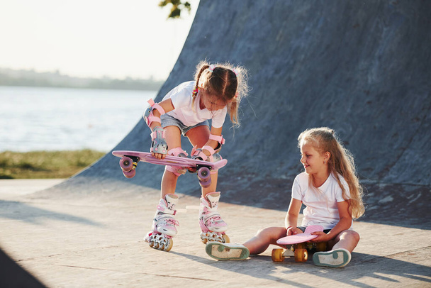 Trying new skate. Two cute female kids have fun outdoors in the park. - Zdjęcie, obraz