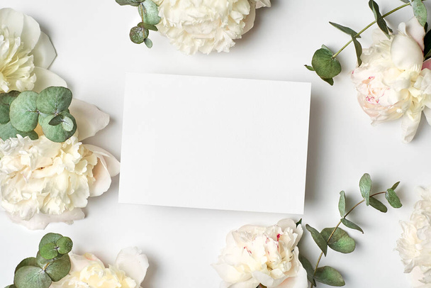 Tarjeta de felicitación maqueta con espacio para copias y flores de peonía blanca y eucalipto sobre fondo blanco - Foto, Imagen