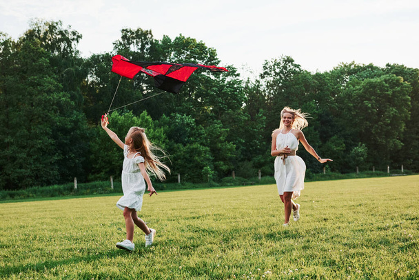 Nice green colors. Mother and daughter have fun with kite in the field. Beautiful nature. - Foto, Imagen