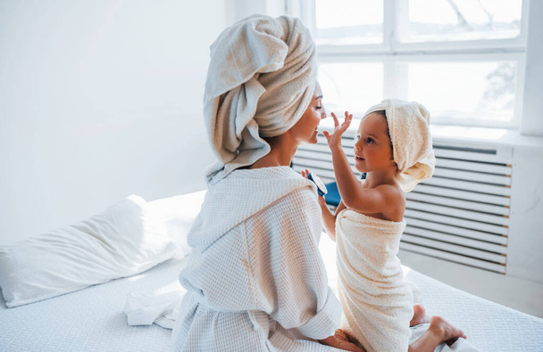 Using cream to clear skin. Young mother with her daugher have beauty day indoors in white room. - Foto, imagen