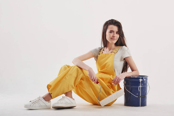 Ready for the work. Brunette woman in yellow uniform sitting against white background in the studio. - Photo, image