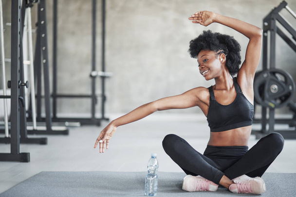 Doing some yoga stretches. African american woman with curly hair and in sportive clothes have fitness day in the gym. - Foto, Bild