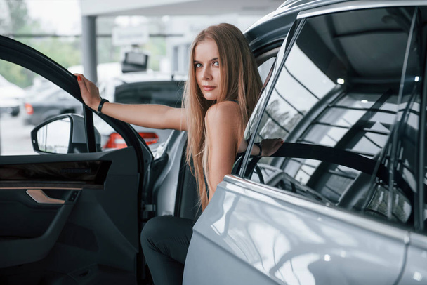 Opening the door. Girl and modern car in the salon. At daytime indoors. Buying new vehicle. - Фото, зображення