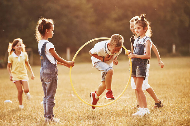 Jumping through the circle fitness tool. Kids having fun in the field. - Zdjęcie, obraz