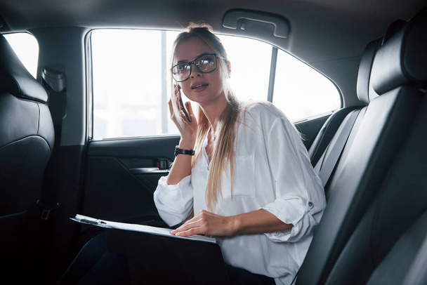 Busy girl. Smart businesswoman sits at backseat of the luxury car with black interior. - Fotografie, Obrázek