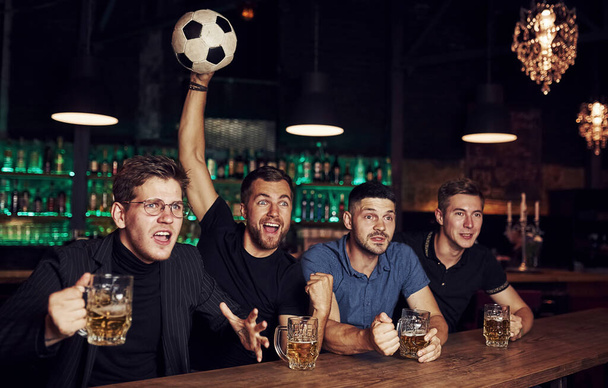 With soccer ball. It's a goal. Celebrating victory. Three sports fans in a bar watching football With beer in hands. - Foto, Imagen