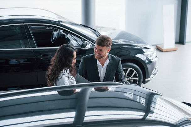 Charming young people. Female customer and modern stylish bearded businessman in the automobile saloon. - Foto, Imagen