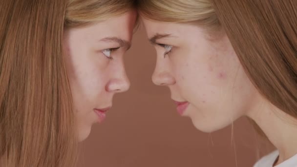 Extreme close up shot of happy twin sisters touching foreheads and smiling while looking at each other and posing isolated on brown background - Footage, Video