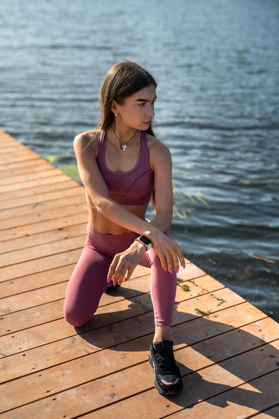 Νεαρή λεπτή γυναίκα κάνει χαλαρωτικές ασκήσεις κοντά στη λίμνη. έννοια του υγιεινού τρόπου ζωής - Φωτογραφία, εικόνα