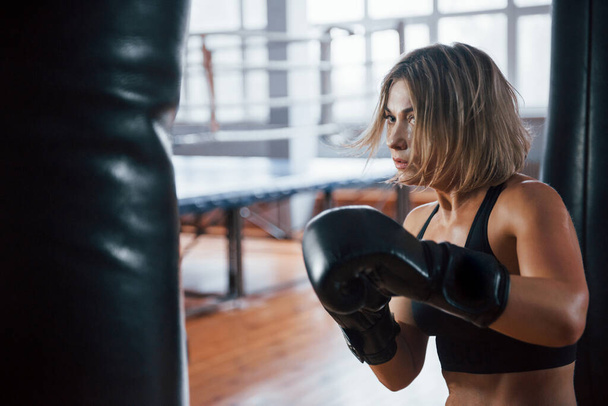 Sweat on the skin. Female boxer is punching the bag. Blonde have exercise in the gym. - Foto, Imagem