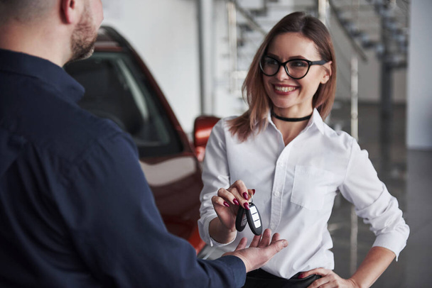 Anahtarları adama vermek için. Gözlüklü ve beyaz gömlekli kadın kırmızı otomobilin yanında duruyor.. - Fotoğraf, Görsel