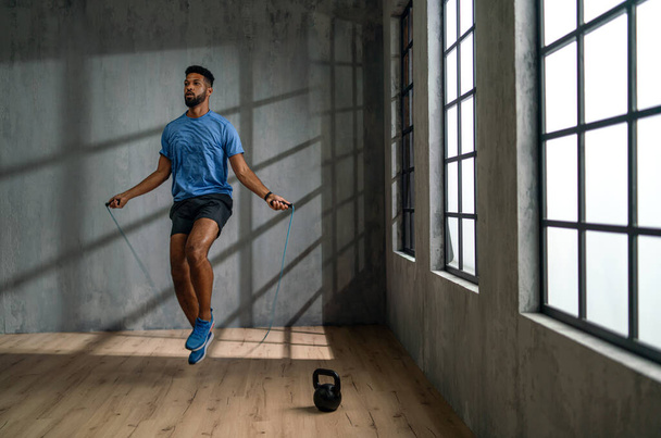 Young African American sportsman using jumping rope indoors, workout training concept. - Foto, afbeelding