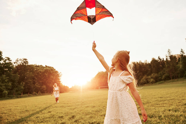 Woman is going to the child. Mother and daughter have fun with kite in the field. Beautiful nature. - Φωτογραφία, εικόνα