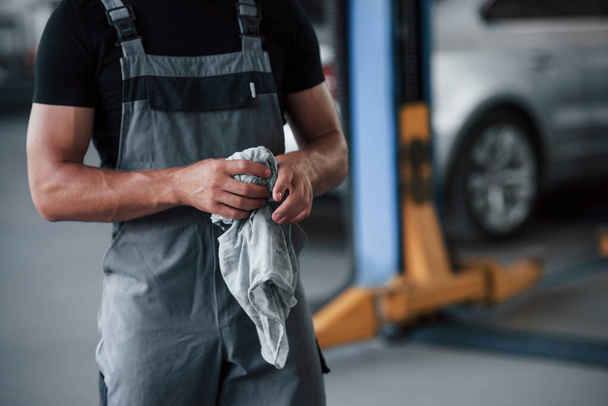 Particle view. Man in black shirt and grey uniform stands in garage after repairing broken car. - Φωτογραφία, εικόνα