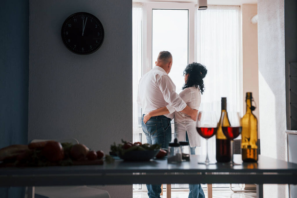 True emotions. Senior man and his wife in white shirt have romantic dinner on the kitchen. - Foto, afbeelding