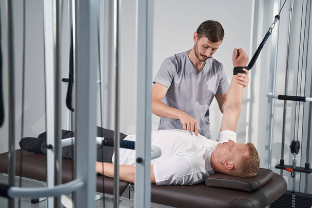 Man exercises on decompression trainer in with physiotherapist help - Foto, imagen