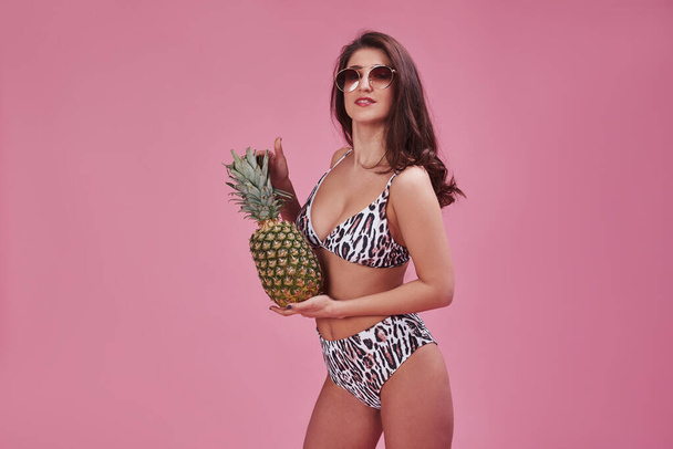 Fresh fruit. Stylish beautiful young girl in bikini stands and posing in the studio. - Фото, изображение