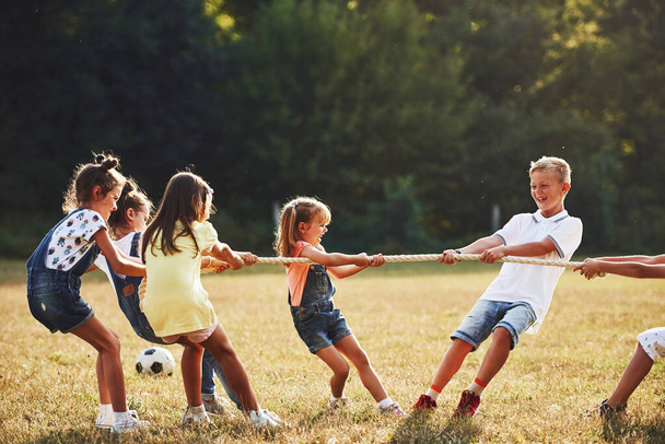 Kids playing tug of war game in the beautiful meadow at sunny day. - Foto, Imagem