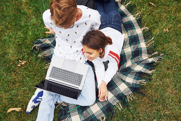 Top view. Young couple sits on green grass on the field with their laptop. - Foto, afbeelding