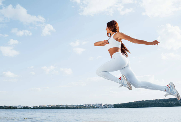 Up in the sky. Female runner in white sportive clothes doing fitness. - Foto, imagen