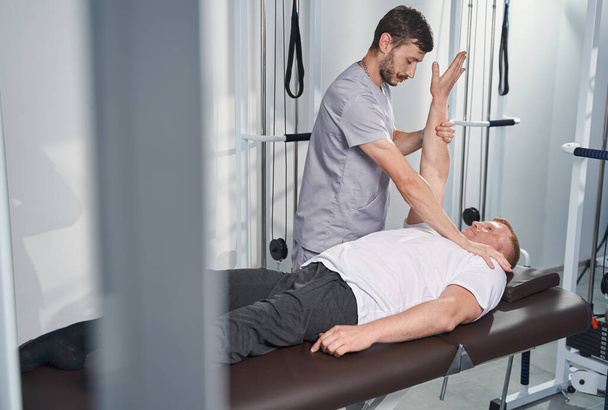L'uomo fisioterapista controlla la mano del paziente maschile sul tavolo da massaggio - Foto, immagini