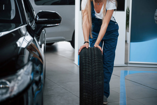 Ready for replacement. Woman walks with brand new wheel to the car. Conception of repair. - Foto, Imagem