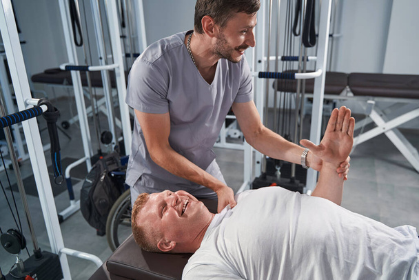 Man therapeut behandelt patiëntenhand op massagetafel. Masseur in uniform - Foto, afbeelding