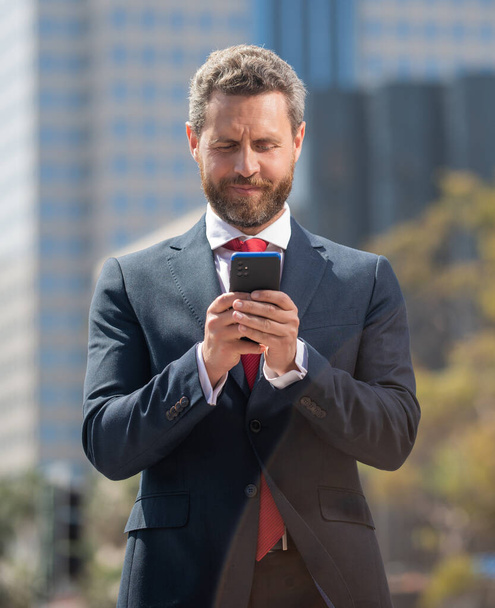 επιτυχημένος επιχειρηματίας με κοστούμι κουβεντιάζοντας στο τηλέφωνο στέκεται υπαίθρια, κυβερνοΔευτέρα - Φωτογραφία, εικόνα