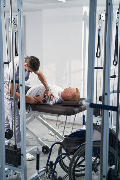 Terapeuta coloca eletroestimulador eletrodos no homem com braço de deficiência - Foto, Imagem