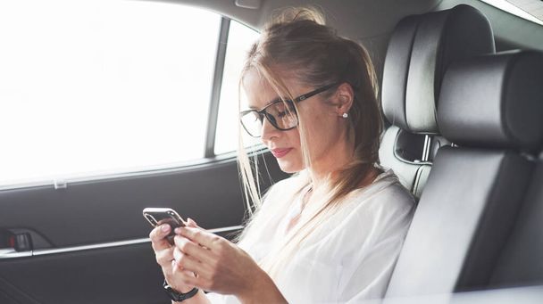 Wireless technologies. Beautiful blonde girl sitting in the new car with modern black interior. - Zdjęcie, obraz