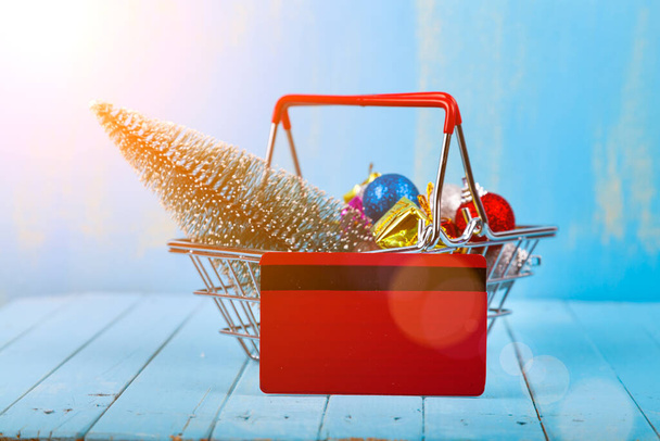 Shopping basket with Christmas gifts, decor and credit card on a blue wooden background. Christmas sale. - Фото, изображение