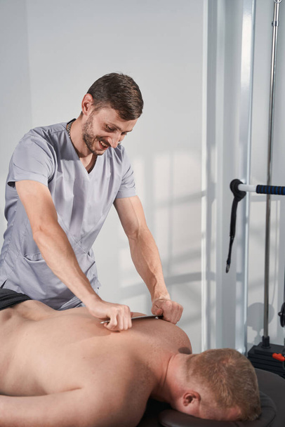 Therapeut macht tiefe Gewebemassage des Menschen Rücken mit IASTM Stahlwerkzeug - Foto, Bild