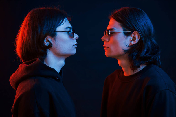 Looking at each other. Creative photo. Portrait of twin brothers. Studio shot in dark studio with neon light. - Fotografie, Obrázek