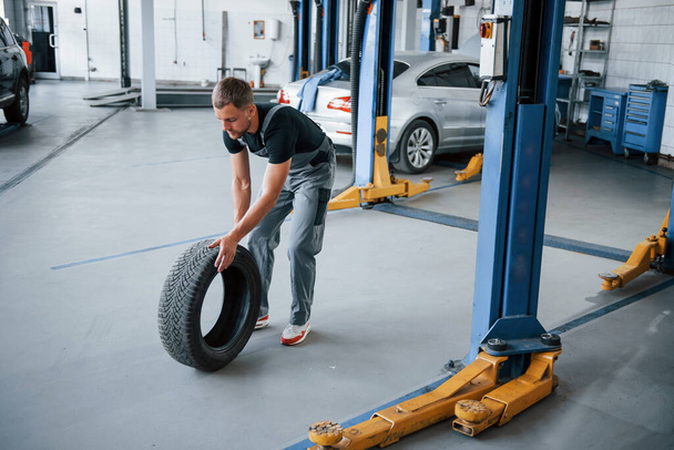 Broken car. Mechanic holds a tire at the repair garage. Replacement of winter and summer tires. - Foto, afbeelding