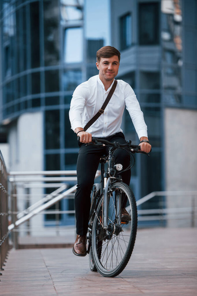 Riding on bike. Businessman in formal clothes with black bicycle is in the city. - 写真・画像