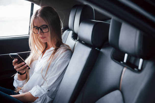 Bored when waiting for the driver. Smart businesswoman sits at backseat of the luxury car with black interior. - Foto, Imagen