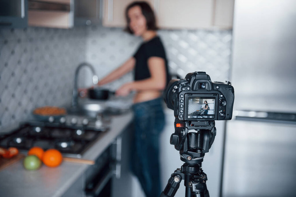 Professional camera on tripod. Girl in the modern kitchen at home at her weekend time in the morning. - Foto, imagen