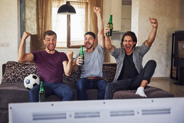 It's a goal. Excited three friends watching soccer on TV at home together. - Zdjęcie, obraz
