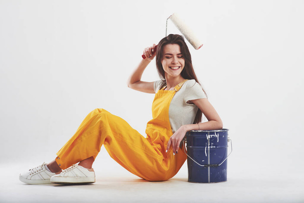 Make it easy. Brunette woman in yellow uniform sits against white background in the studio. - Фото, изображение