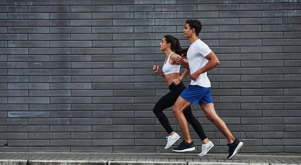 Healthy lifestyle. Man and woman have fitness day and running in the city at daytime near brick wall. - Foto, Imagem