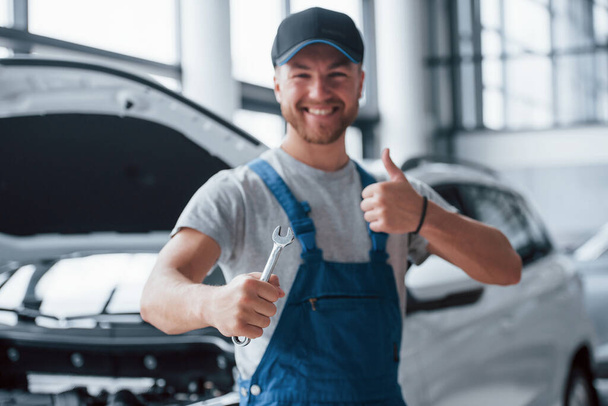 Your car is in good hands. Employee in the blue colored uniform stands in the automobile salon. - Zdjęcie, obraz