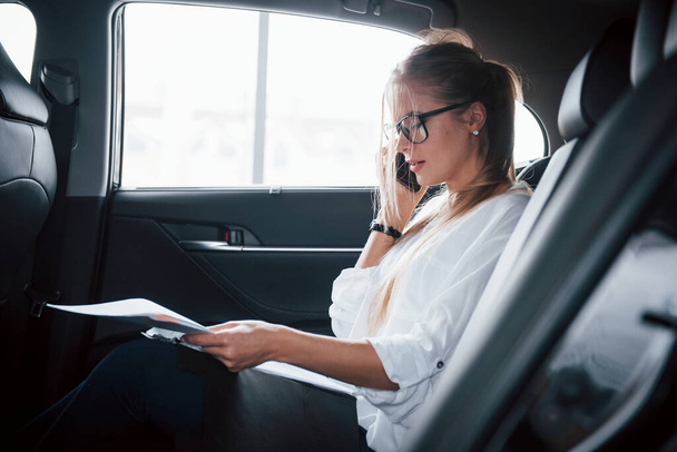 Active conversation. Smart businesswoman sits at backseat of the luxury car with black interior. - Foto, Imagen