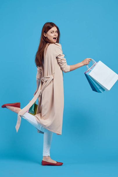 cheerful woman with multicolored bags posing blue background - 写真・画像