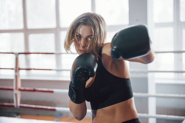 Shadow fighting. Female sportswoman training in the boxing ring. In black colored clothes. - 写真・画像